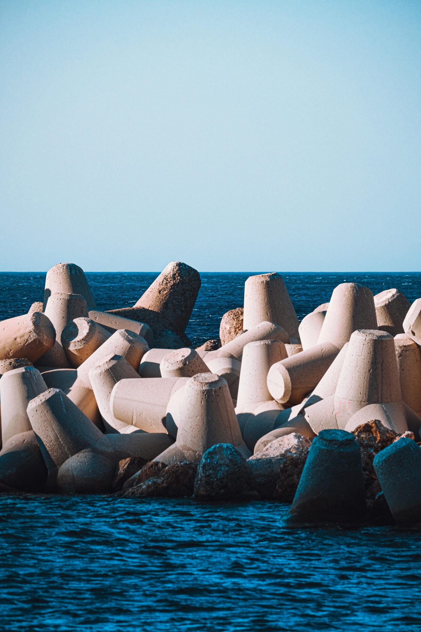 Concrete tetrapods providing coastal protection along a vibrant blue ocean shoreline under clear skies.