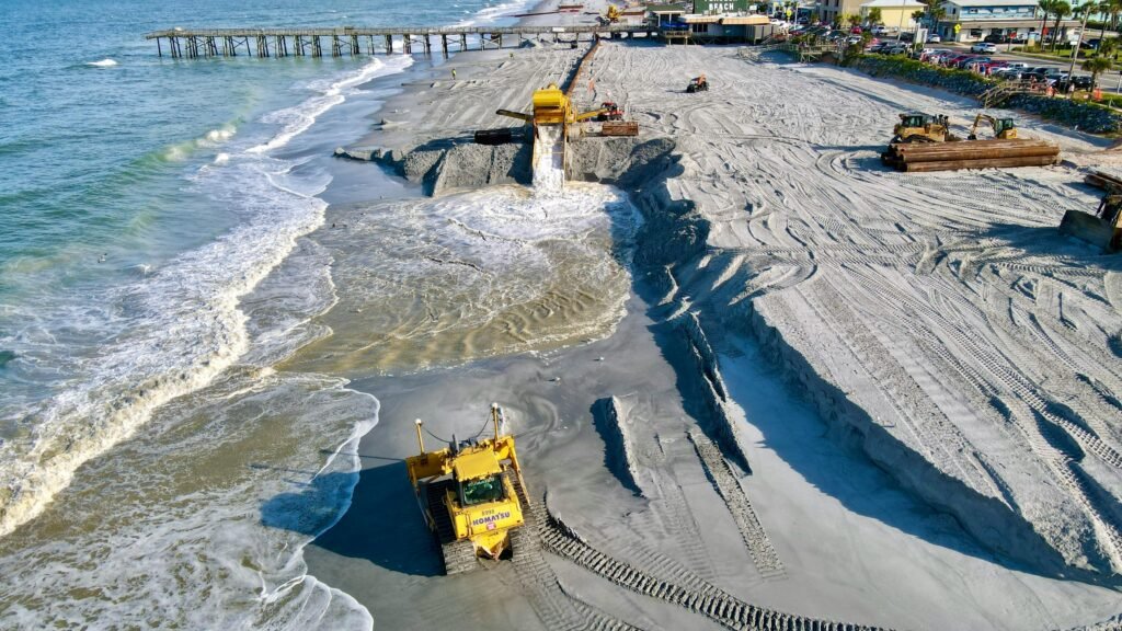 Aerial view of beach reclamation project with construction vehicles reshaping the coastline.